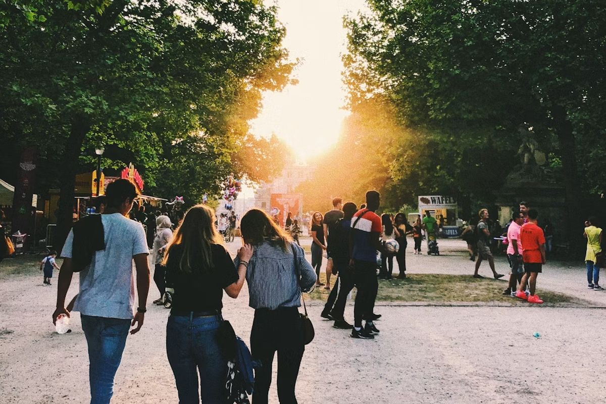 People walking through a tree-lined park toward the evening sun